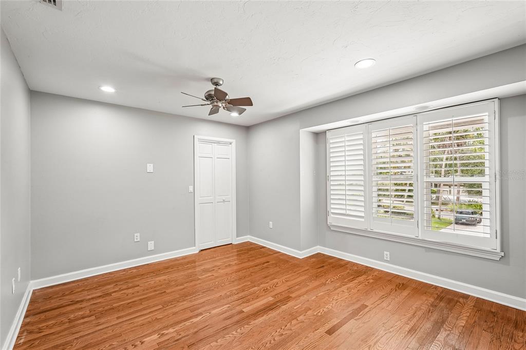 An empty bedroom with light gray walls, hardwood floors, a ceiling fan, and plantation shutters — 1675 LANDINGS LANE, SARASOTA, FL