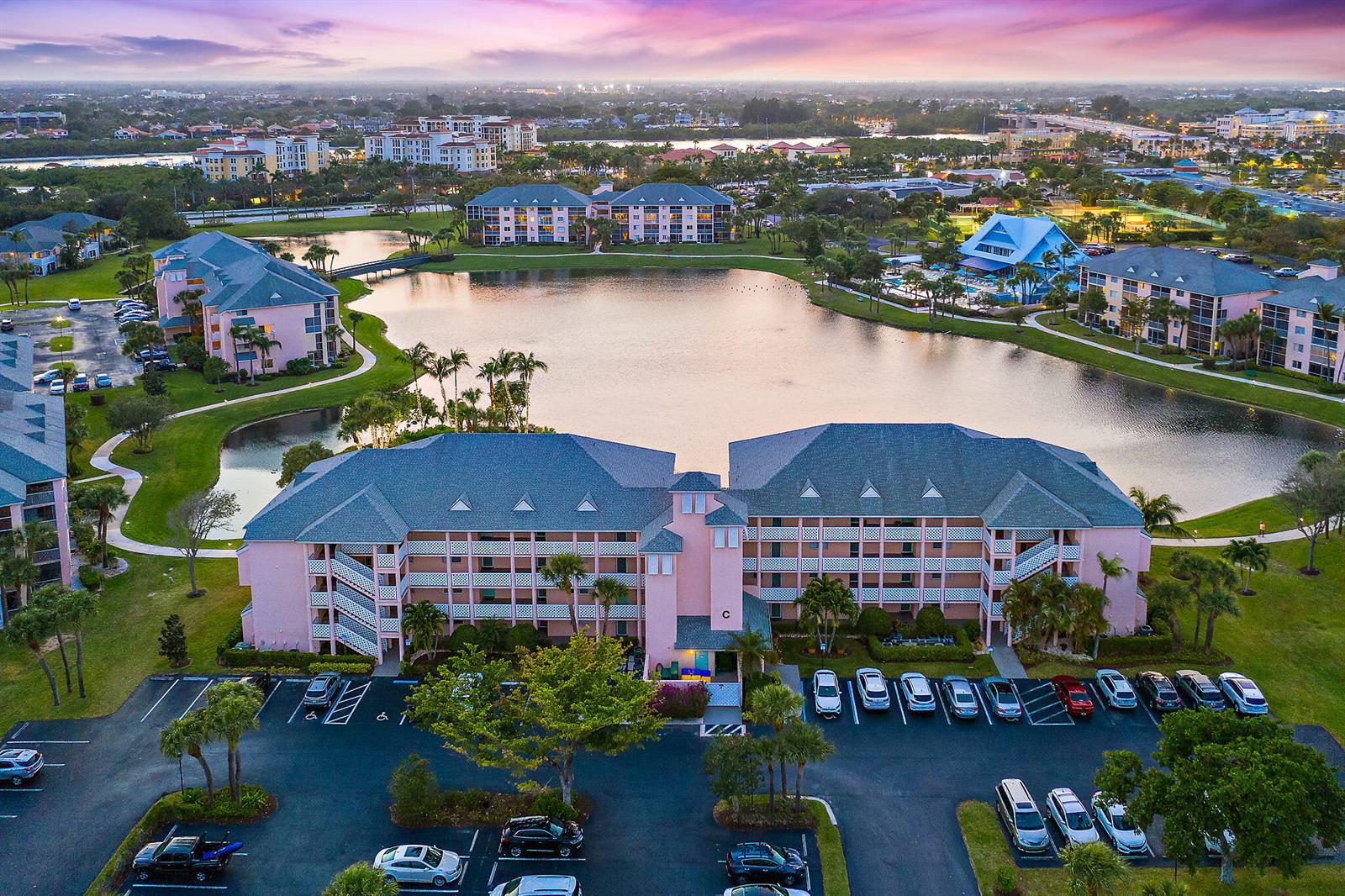 An aerial view shows pink apartment buildings surrounding a central lake at sunset — 353 S Us Highway 1 # C203, Jupiter FL 33477, JUPITER, FL