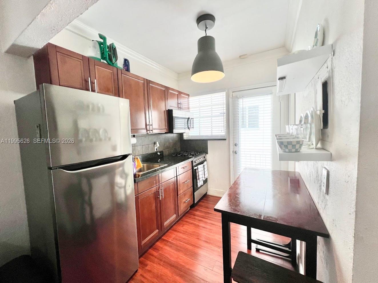 A kitchen features wood-look flooring, white walls, a stainless steel refrigerator, and a dining bench — 330 74th St # 5, Miami Beach FL 33141, MIAMI BEACH, FL