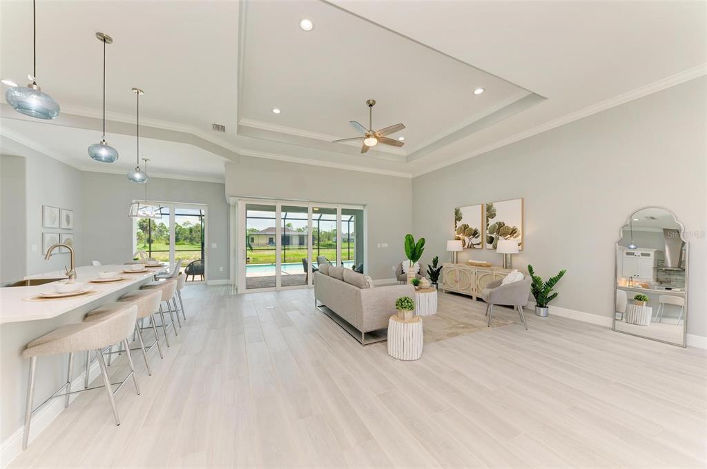 An open-concept living room and kitchen area features light wood flooring, a tray ceiling, and sliding glass doors — 777 BOUNDARY BOULEVARD, ROTONDA WEST, FL