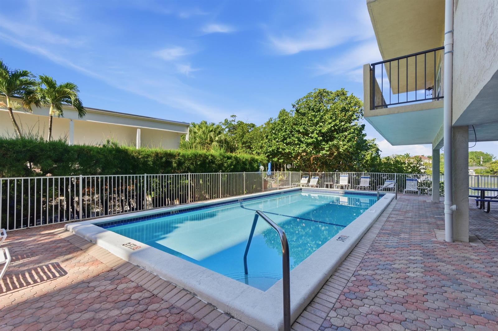 A rectangular swimming pool sits on a brick patio next to a multi-story building — 3581 S Ocean Boulevard Apt 4e, South Palm Beach FL 33480, SOUTH PALM BEACH, FL
