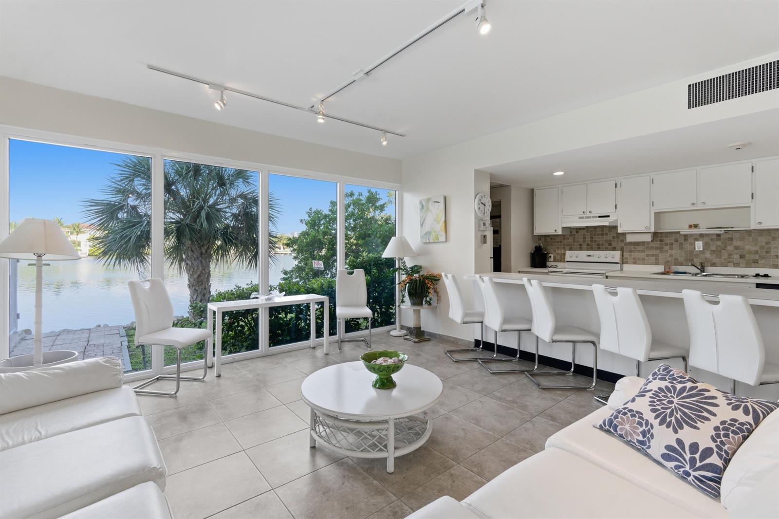 A living room and kitchen area with tile floors, white furniture, and large windows overlooking water — 3581 S Ocean Boulevard Apt 4e, South Palm Beach FL 33480, SOUTH PALM BEACH, FL
