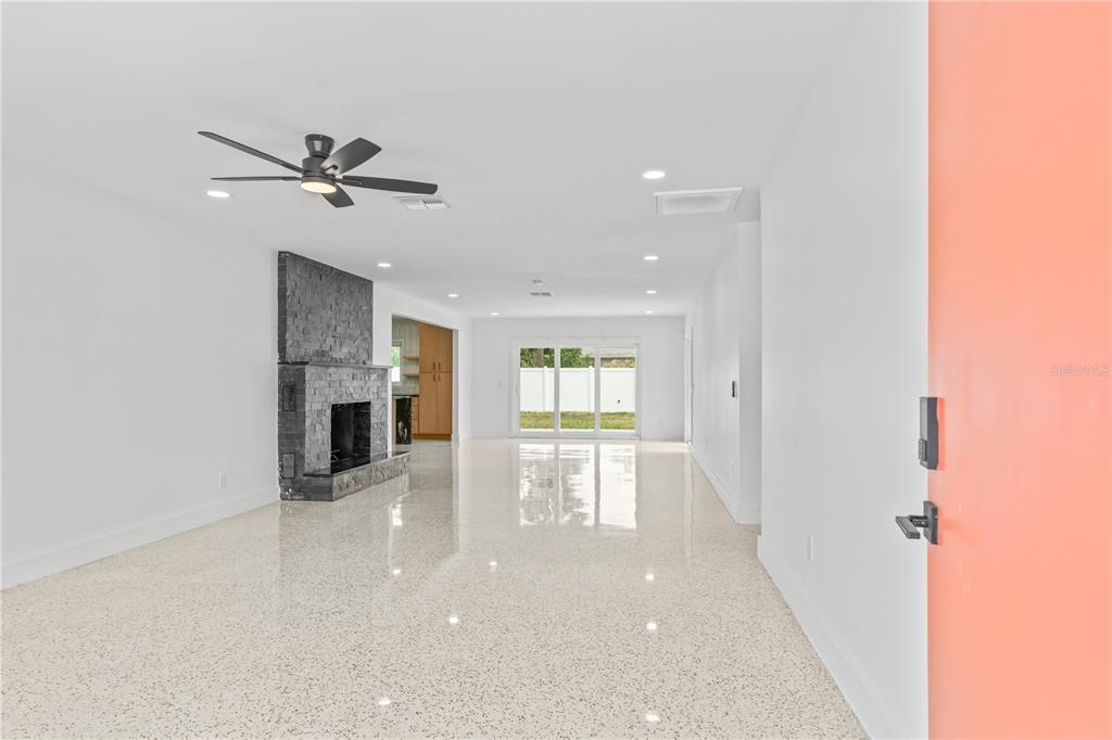 A living room features a stone fireplace, terrazzo flooring, and a view of the backyard — 123 8TH STREET, BELLEAIR BEACH, FL
