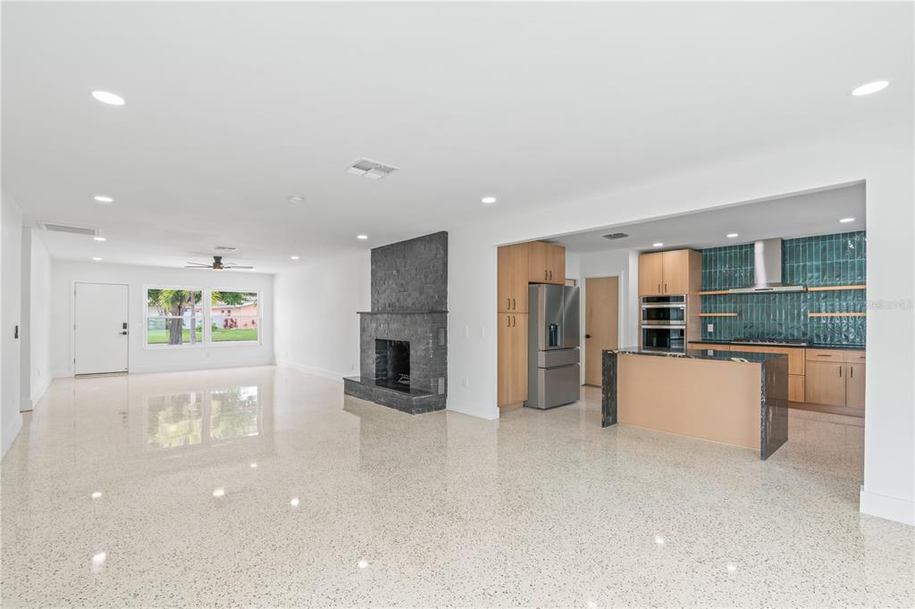 An open-concept living room features a stone fireplace, polished terrazzo floors, and a modern kitchen — 123 8TH STREET, BELLEAIR BEACH, FL