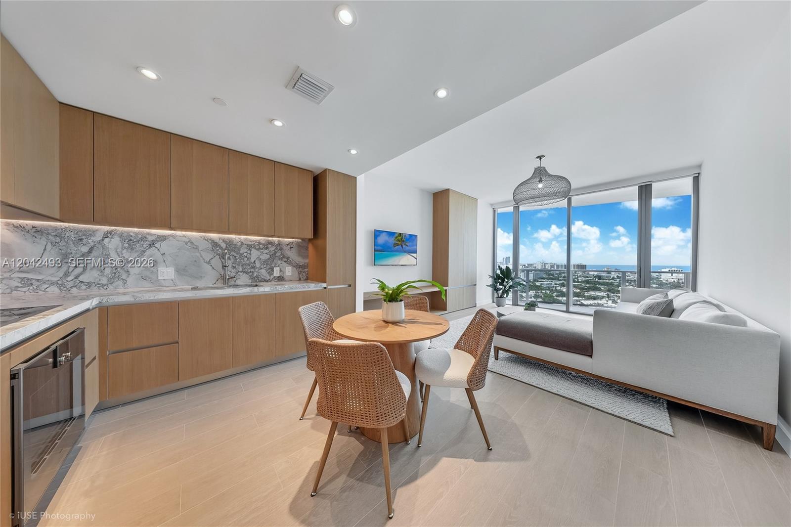 A modern studio apartment features a kitchen with wood cabinetry, a dining area, and a sofa — 500 Alton Rd # 1906, Miami Beach FL 33139, MIAMI BEACH, FL