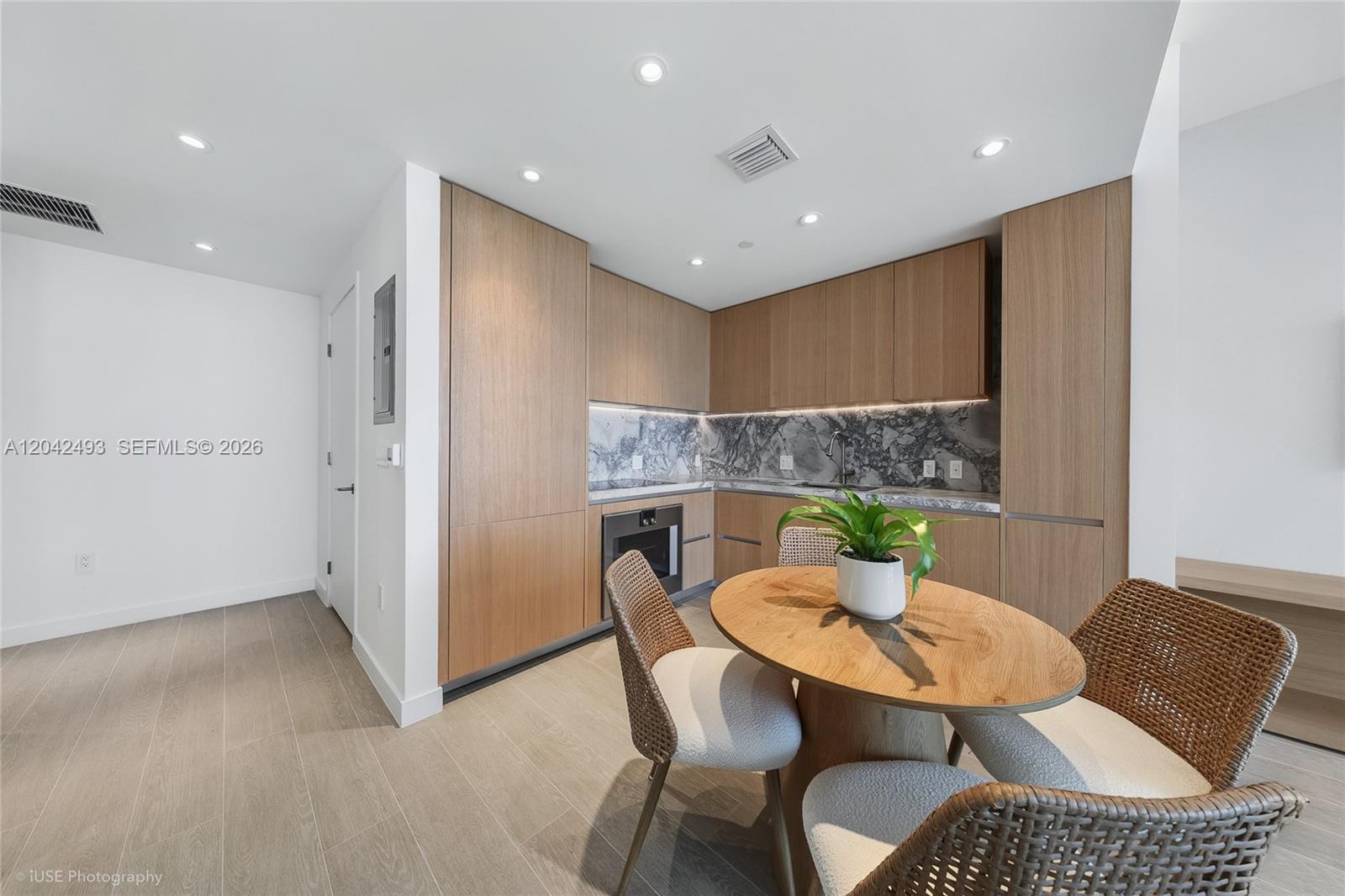 A modern kitchen features light wood cabinetry, a marble backsplash, and a small dining area — 500 Alton Rd # 1906, Miami Beach FL 33139, MIAMI BEACH, FL
