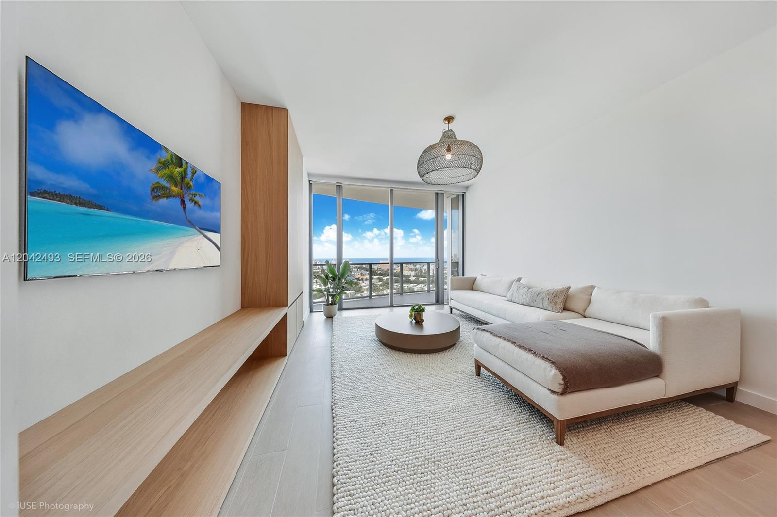 A modern living room features a white sectional sofa, wood media console, and balcony view — 500 Alton Rd # 1906, Miami Beach FL 33139, MIAMI BEACH, FL