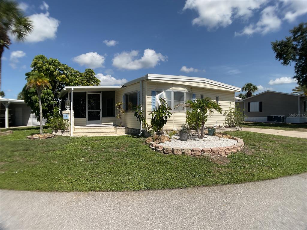 A light yellow manufactured home features a screened-in porch and a landscaped front yard — 2100 KINGS HIGHWAY TRAIL UNIT 116, PORT CHARLOTTE, FL