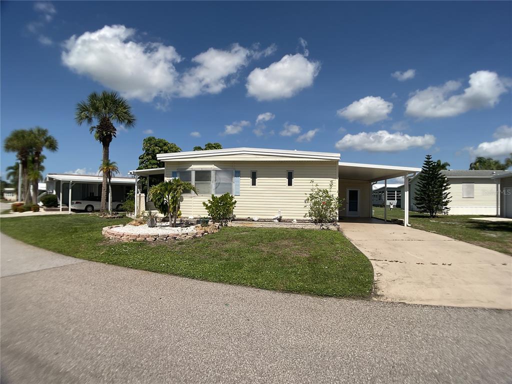 A single-story mobile home with light siding, a carport, and a landscaped front yard — 2100 KINGS HIGHWAY TRAIL UNIT 116, PORT CHARLOTTE, FL