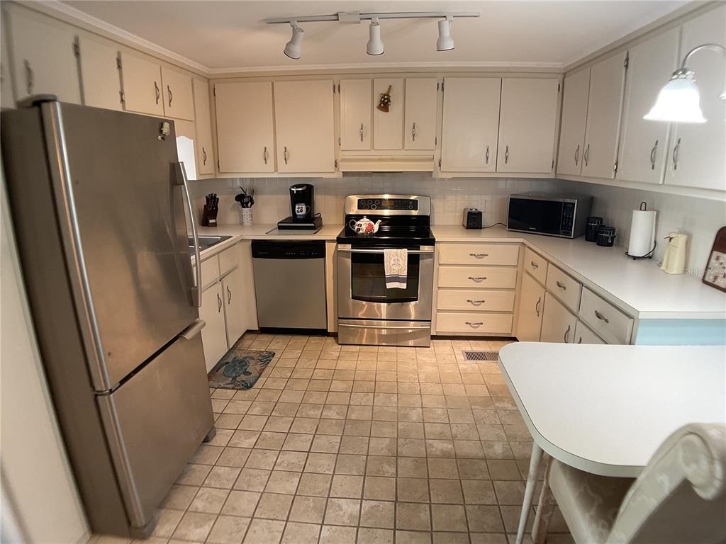 A kitchen features stainless steel appliances, off-white cabinetry, and light-colored tile flooring — 2100 KINGS HIGHWAY TRAIL UNIT 116, PORT CHARLOTTE, FL