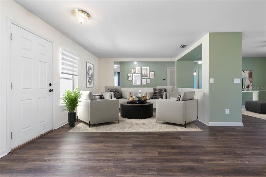 A living room with wood-look flooring, light green accent walls, and virtual furniture staging — 27 WOOD ARBOR LANE, PALM COAST, FL
