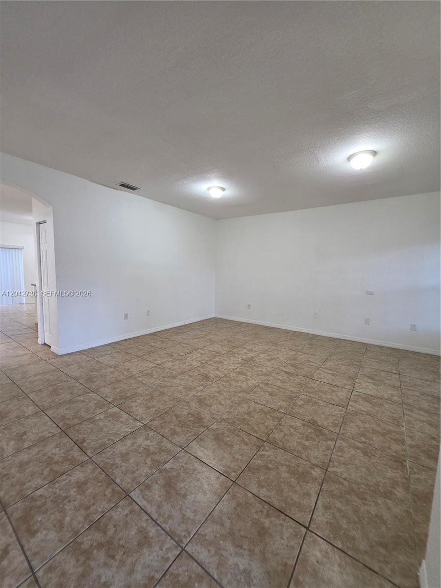 An empty room features white walls, beige tile flooring, and two ceiling-mounted light fixtures — 4906 SW 141st Ave # 4, Miramar FL 33027, MIRAMAR, FL