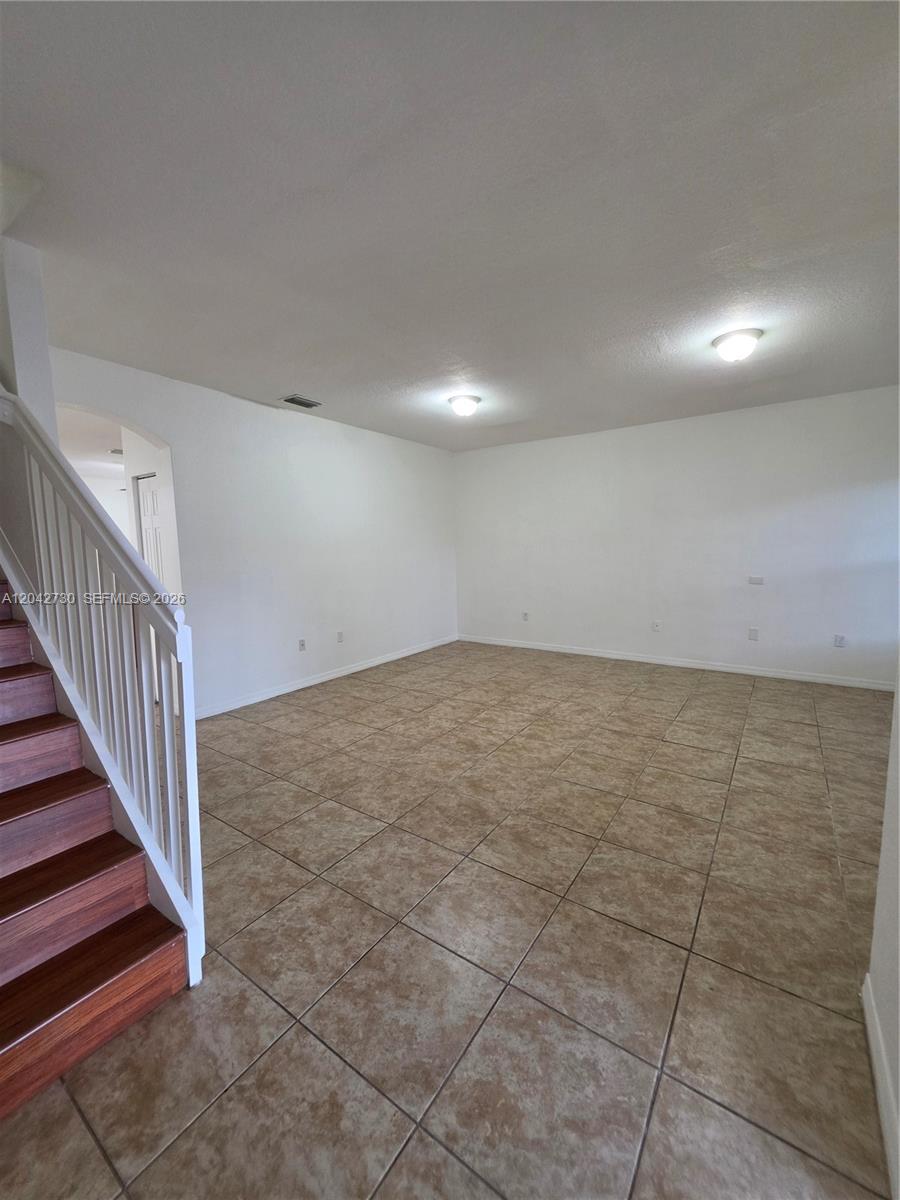 An empty living room features tan tile flooring, white walls, and a wooden staircase — 4906 SW 141st Ave # 4, Miramar FL 33027, MIRAMAR, FL