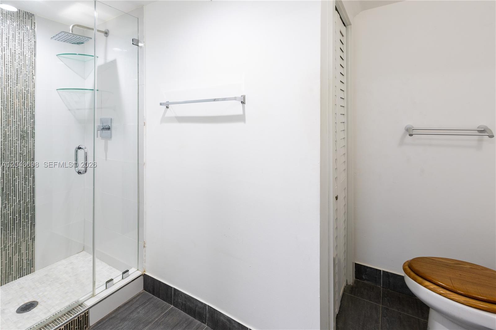 A bathroom features a glass-enclosed shower, a toilet with a wooden seat, and tiled flooring — 4538 SW 1st St # 3, Miami FL 33134, MIAMI, FL