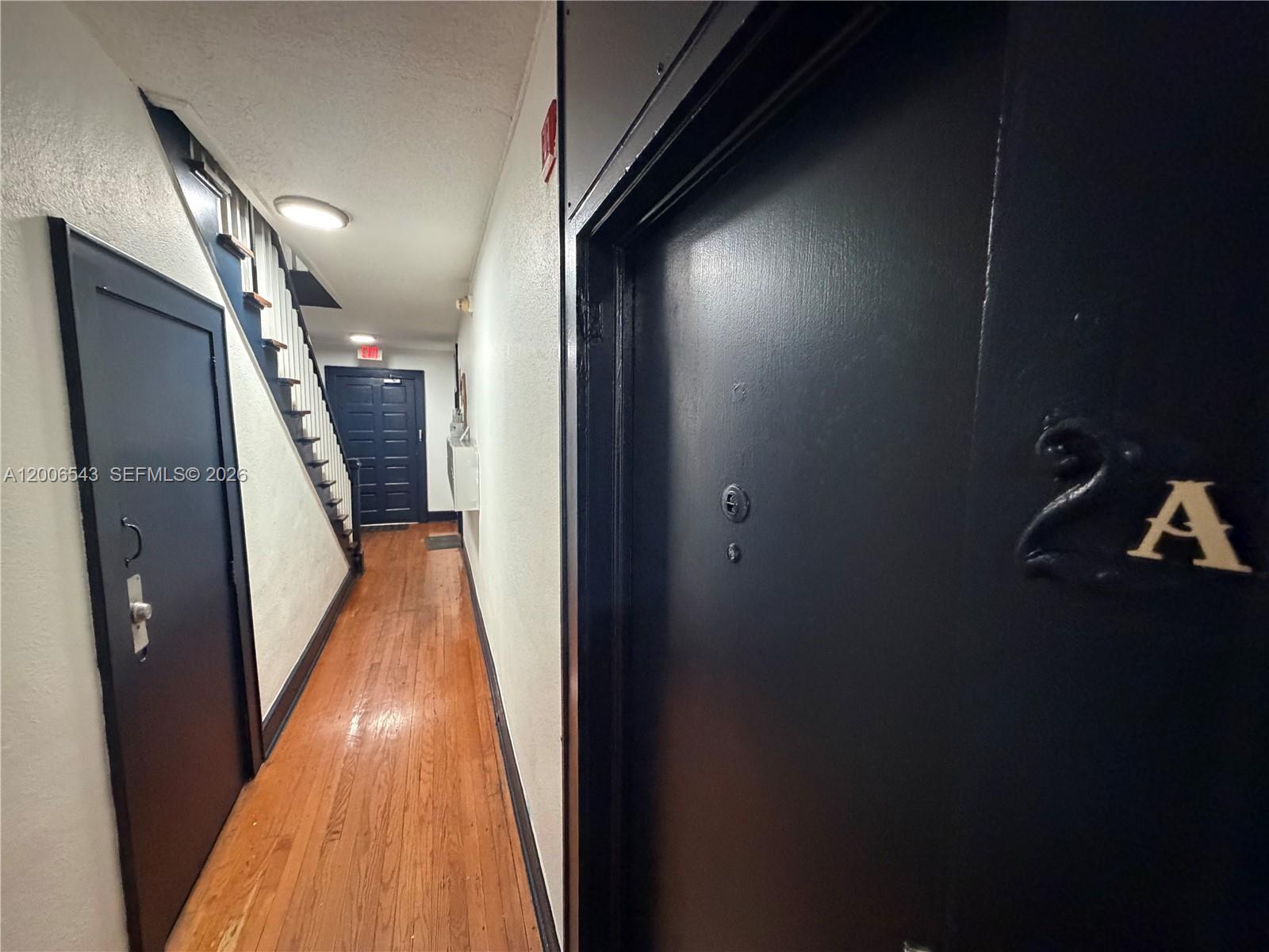 A hallway features hardwood floors, black doors, and a staircase leading to an exit — 124 Mendoza Ave # 2A, Coral Gables FL 33134, CORAL GABLES, FL