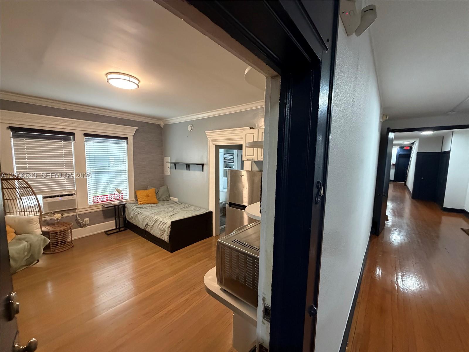 A studio apartment features hardwood floors, a bed, a small kitchen area, and hallway access — 124 Mendoza Ave # 2A, Coral Gables FL 33134, CORAL GABLES, FL
