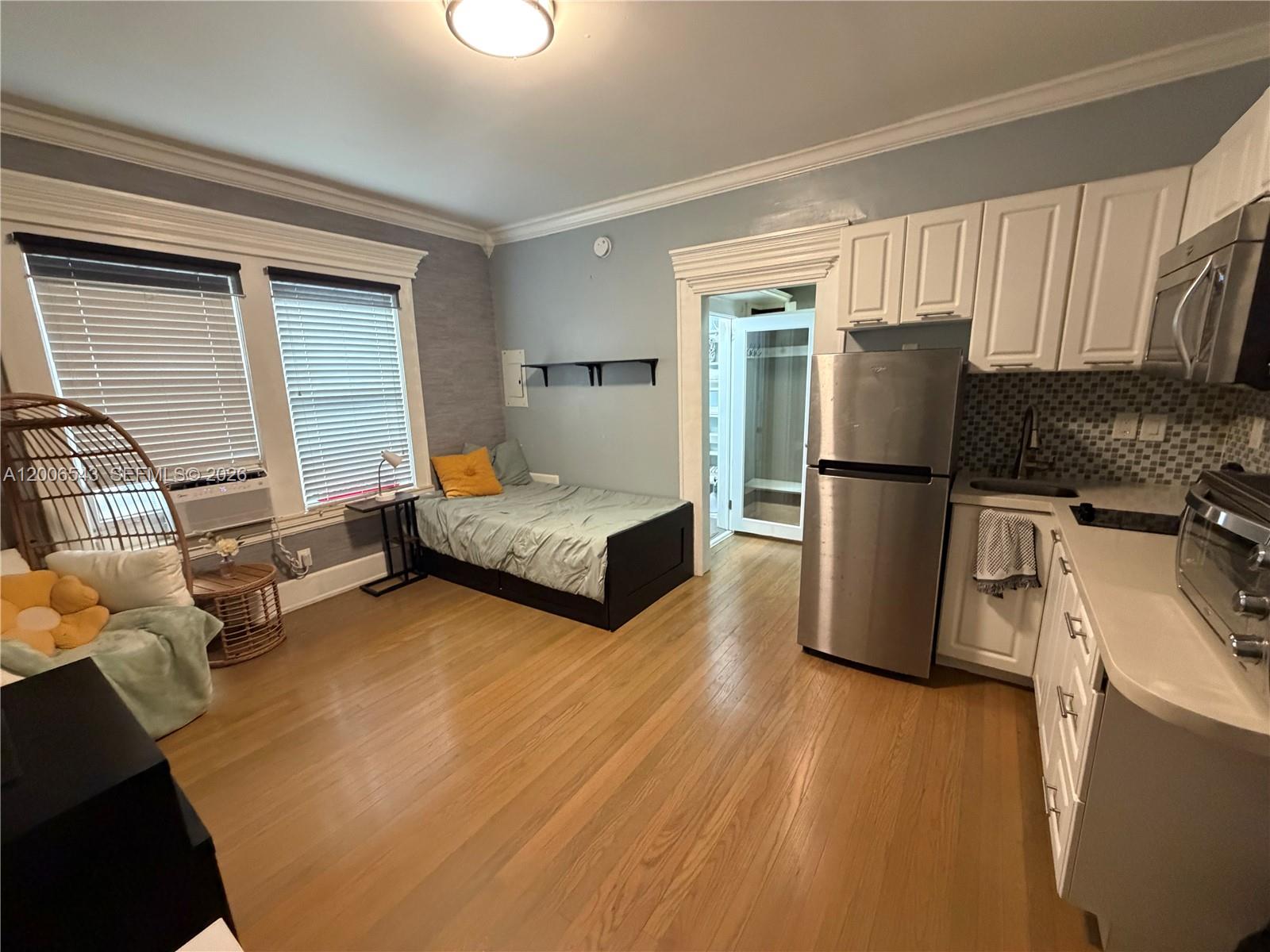 A studio apartment features a bed, kitchen area with stainless steel appliances, and hardwood floors — 124 Mendoza Ave # 2A, Coral Gables FL 33134, CORAL GABLES, FL