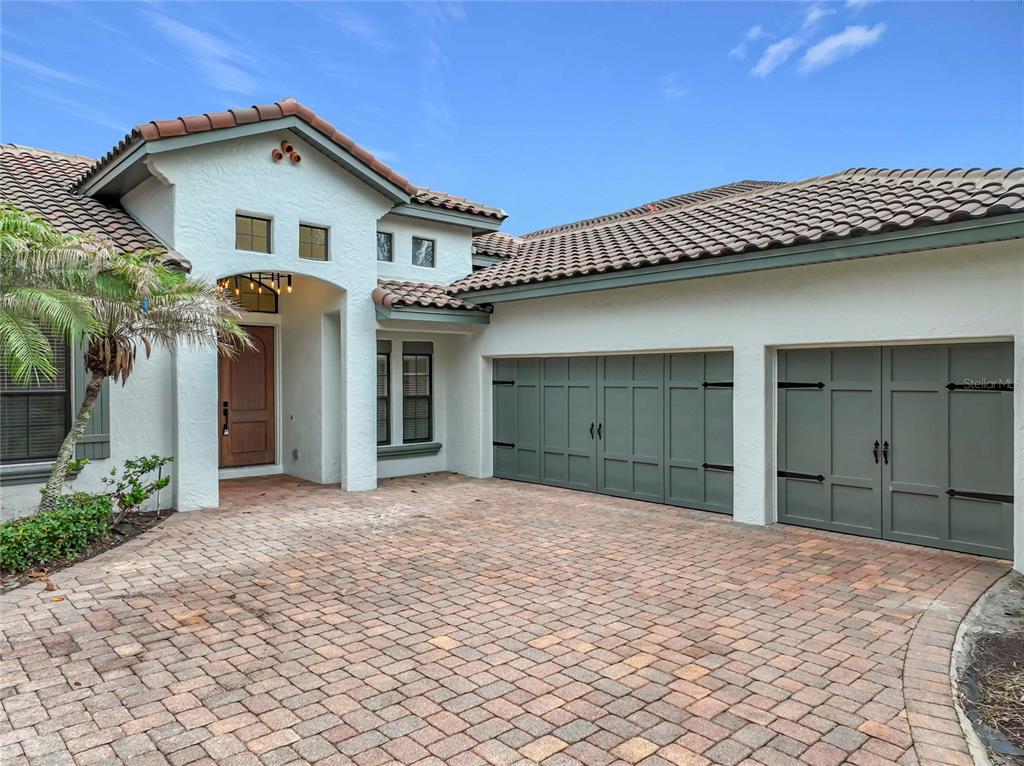A white stucco house features a brown tile roof, green garage doors, and a paver driveway — 7426 POINTE VENEZIA DRIVE, ORLANDO, FL