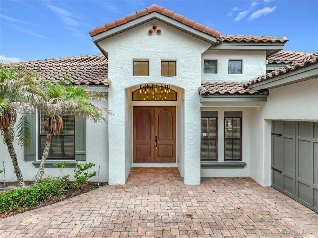 The exterior of a stucco home features a brick paver entryway and double wooden doors — 7426 POINTE VENEZIA DRIVE, ORLANDO, FL