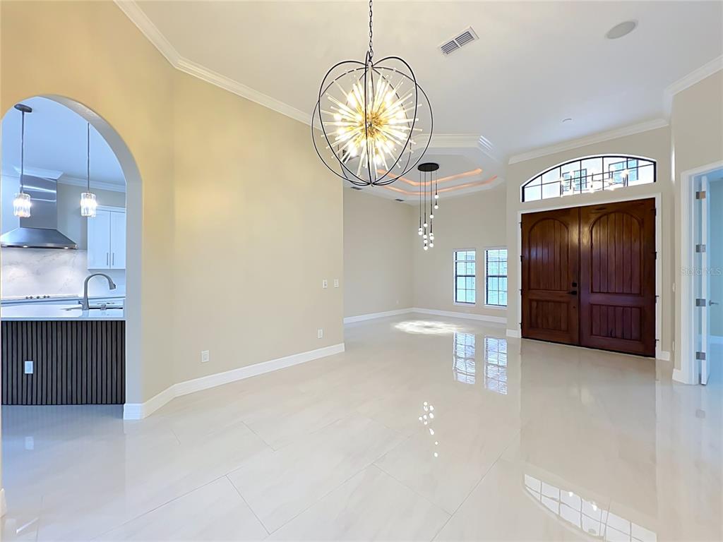 A bright, open-concept foyer and dining area featuring tile floors and two modern chandeliers — 7426 POINTE VENEZIA DRIVE, ORLANDO, FL