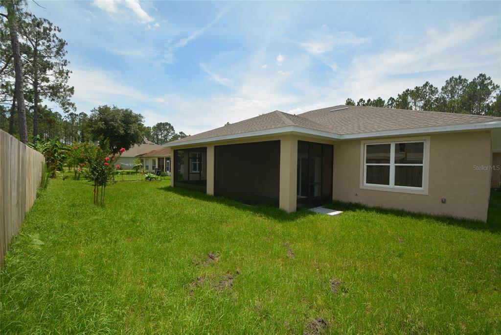 A backyard view of a house with a screened-in patio and a wooden fence — 87 SEA TRAIL UNIT A, PALM COAST, FL