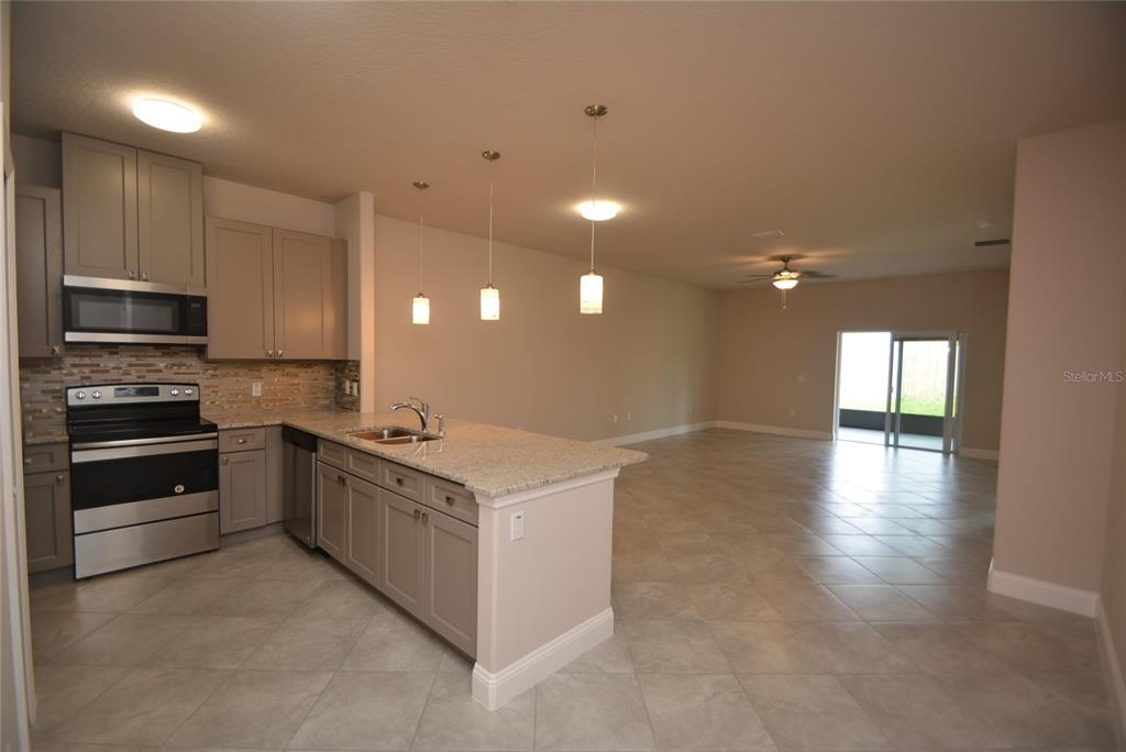 A kitchen with gray cabinets, granite countertops, and stainless steel appliances opens to a living area — 87 SEA TRAIL UNIT A, PALM COAST, FL
