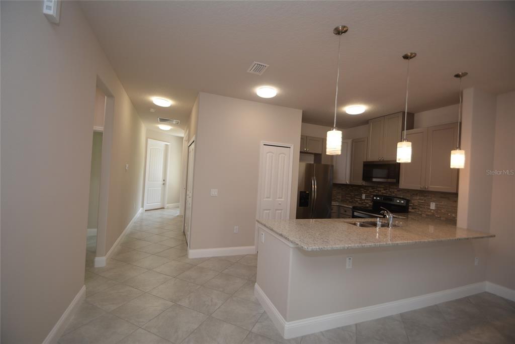 A kitchen with granite countertops and pendant lights opens to a hallway with tiled floors — 87 SEA TRAIL UNIT A, PALM COAST, FL