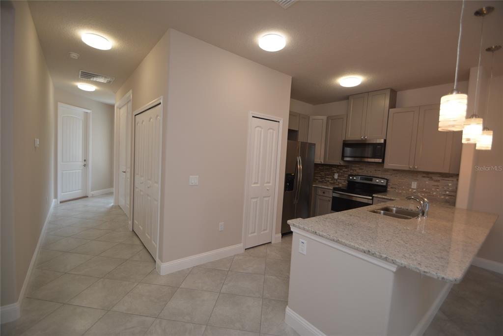 A kitchen with granite countertops, stainless steel appliances, and tile flooring leads to a hallway — 87 SEA TRAIL UNIT A, PALM COAST, FL