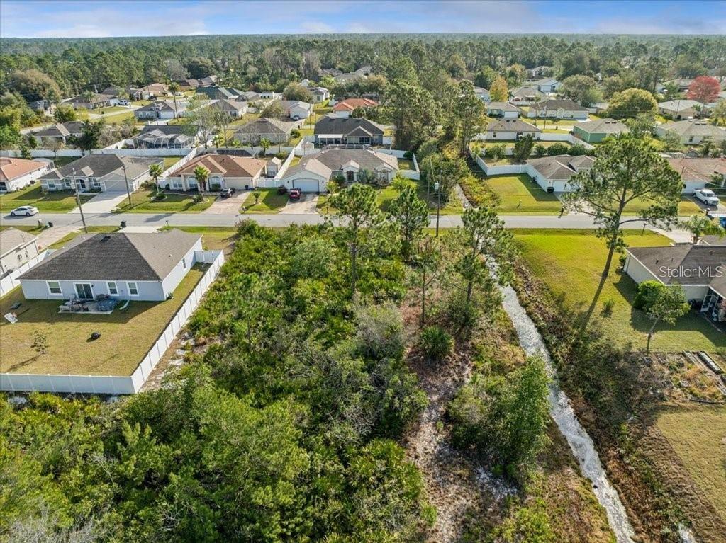 An aerial view shows a vacant, wooded residential lot situated between two houses and a canal — 10 ROCKING LN, PALM COAST, FL