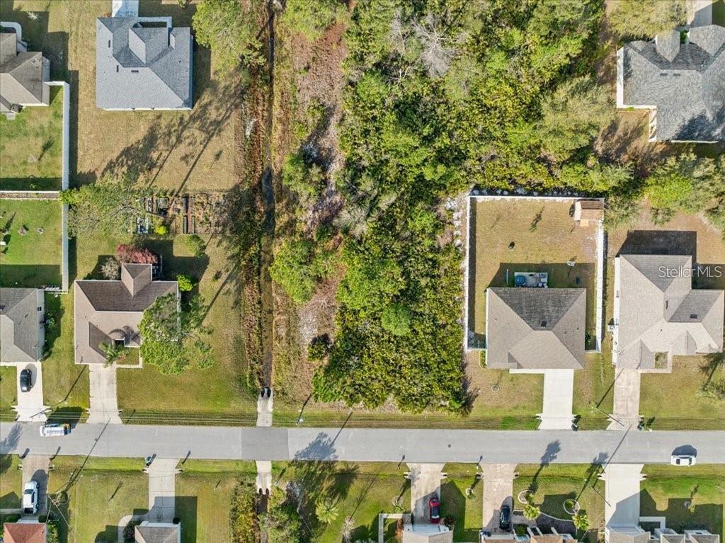 An aerial view shows a vacant, wooded lot situated between two residential houses and a street — 10 ROCKING LN, PALM COAST, FL