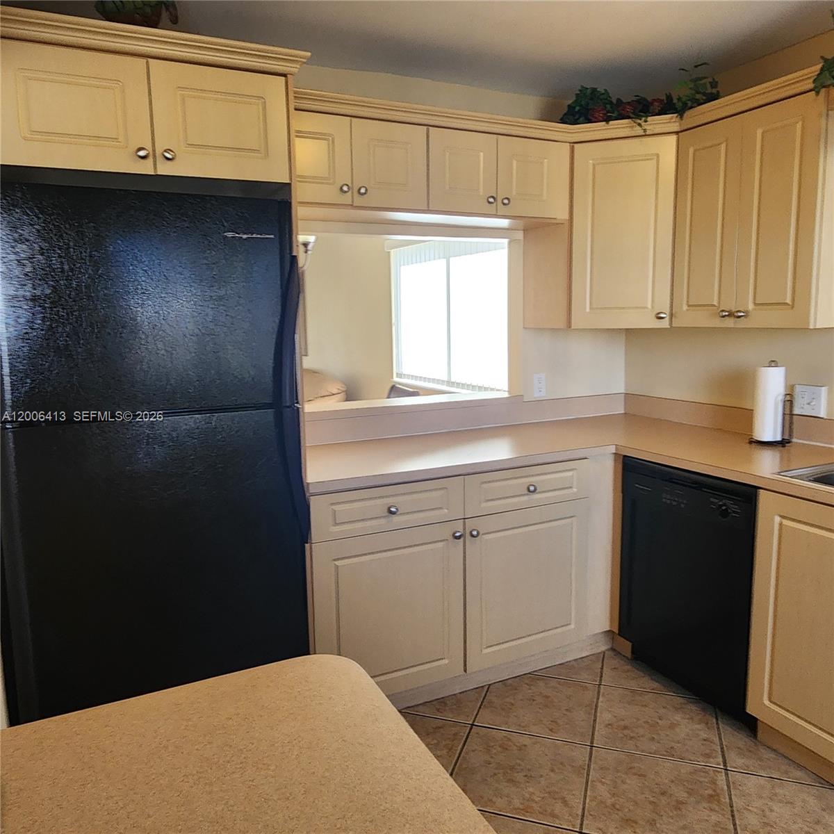 A kitchen features light-colored cabinets, black appliances, tan countertops, and diagonal floor tiles — 16501 Blatt Blvd # 204, Weston FL 33326, WESTON, FL