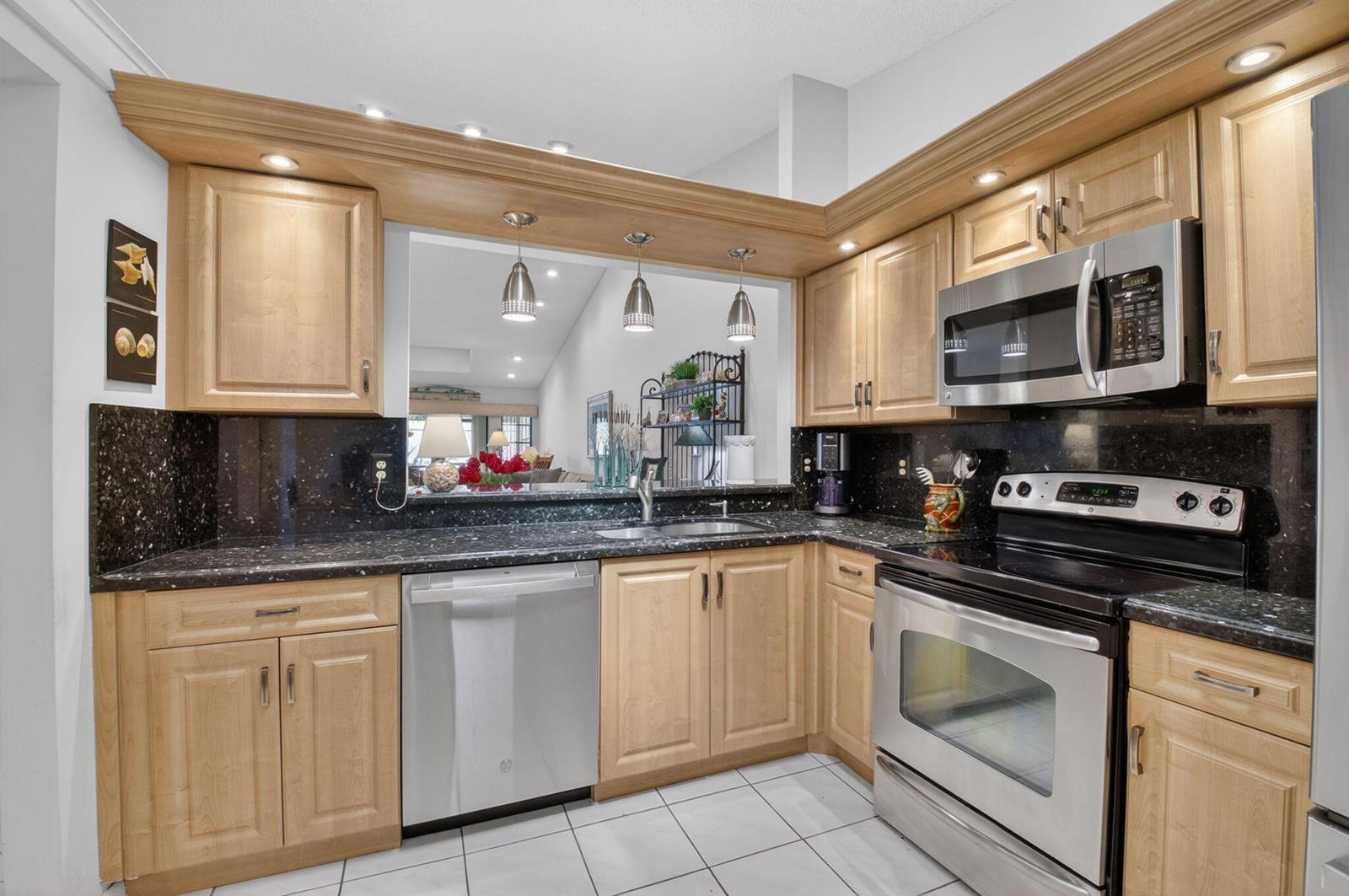 A kitchen with light wood cabinets, black granite countertops, stainless steel appliances, and tile flooring — 10039 Andrea Lane # A, Boynton Beach FL 33437, BOYNTON BEACH, FL