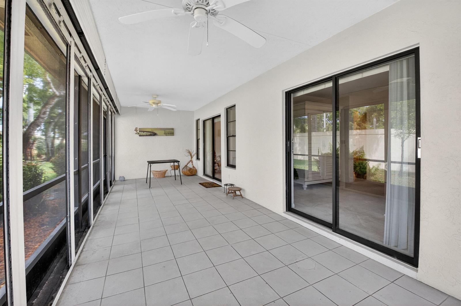 A covered patio features gray tile flooring, white walls, ceiling fans, and large sliding glass doors — 10039 Andrea Lane # A, Boynton Beach FL 33437, BOYNTON BEACH, FL