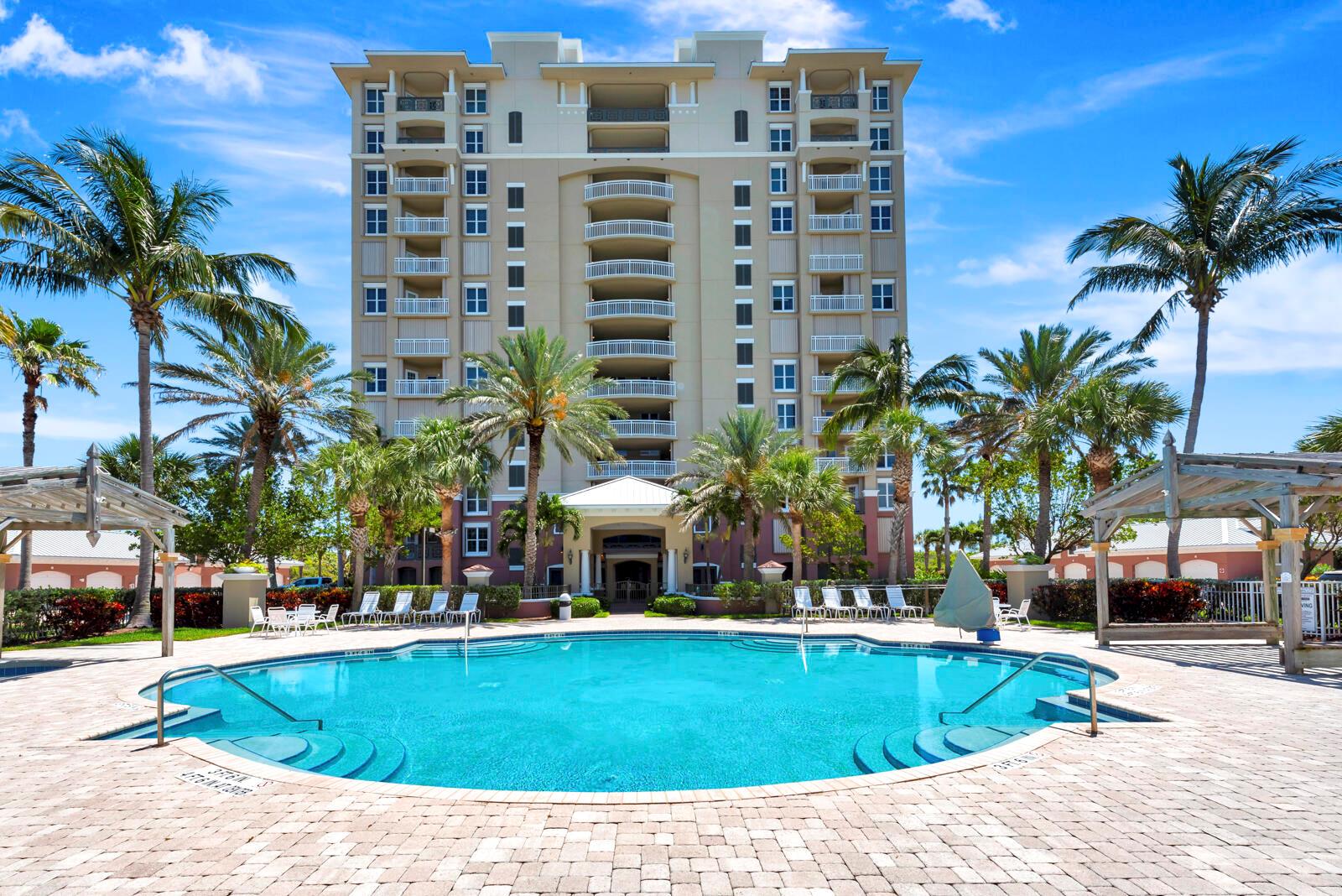 A multi-story residential building stands behind a swimming pool surrounded by palm trees — FORT PIERCE, FL