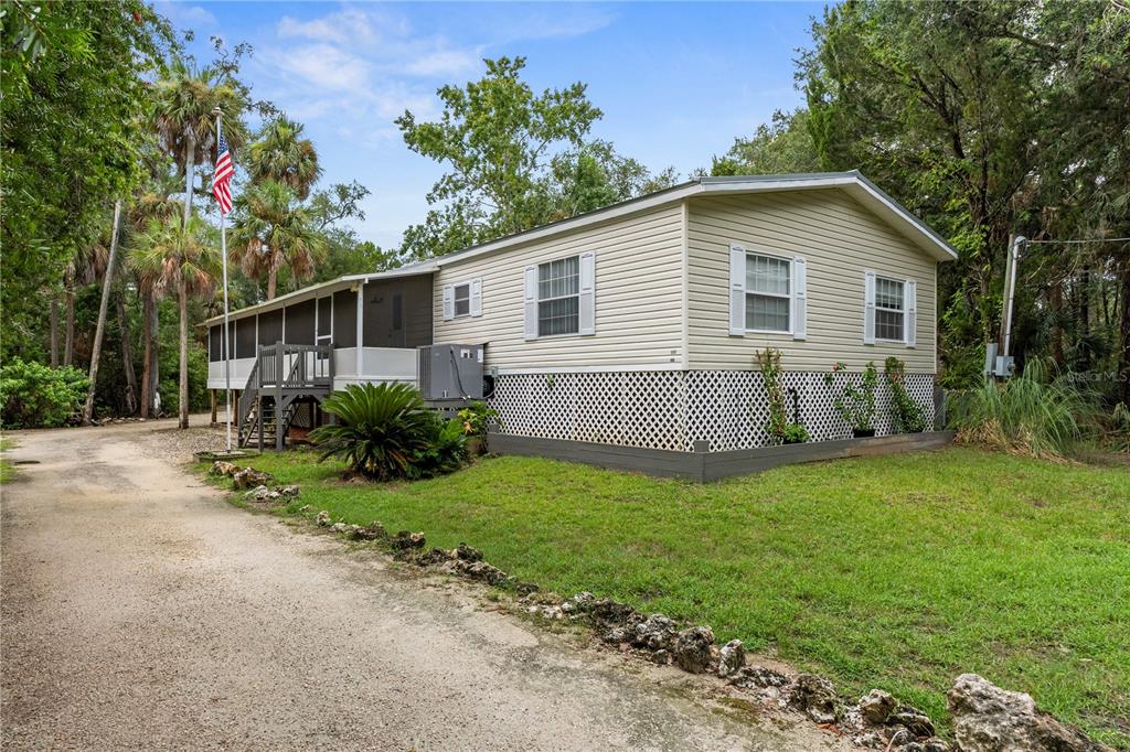 A light-colored mobile home with a screened-in porch sits on a gravel driveway — 11720 W NORTH PLACE, HOMOSASSA, FL