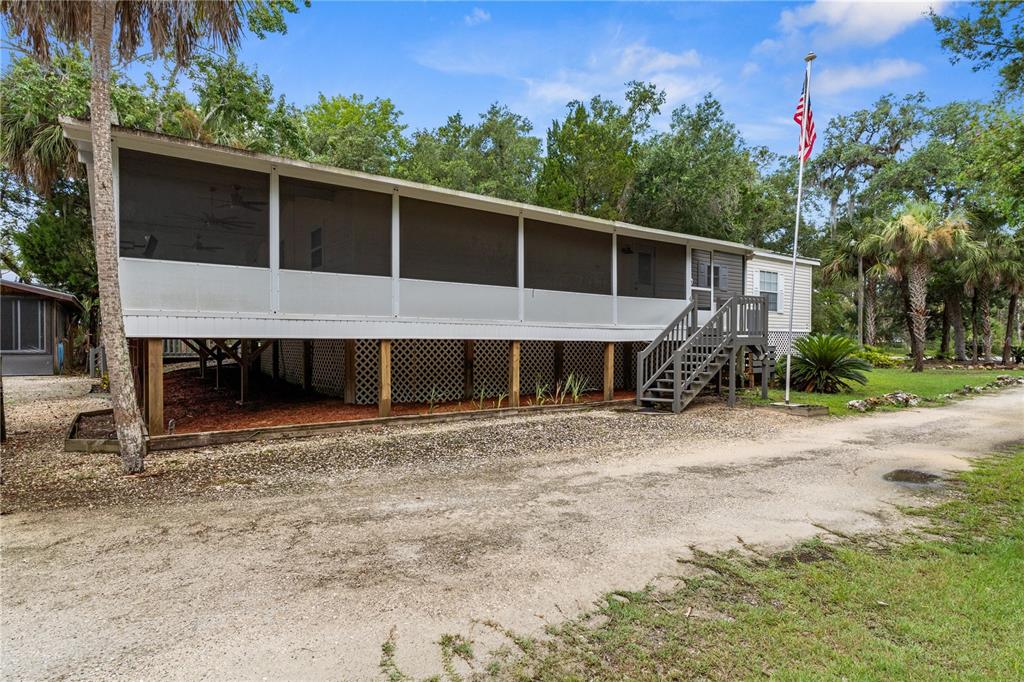An elevated mobile home with a large screened-in porch and stairs sits on a gravel lot — 11720 W NORTH PLACE, HOMOSASSA, FL