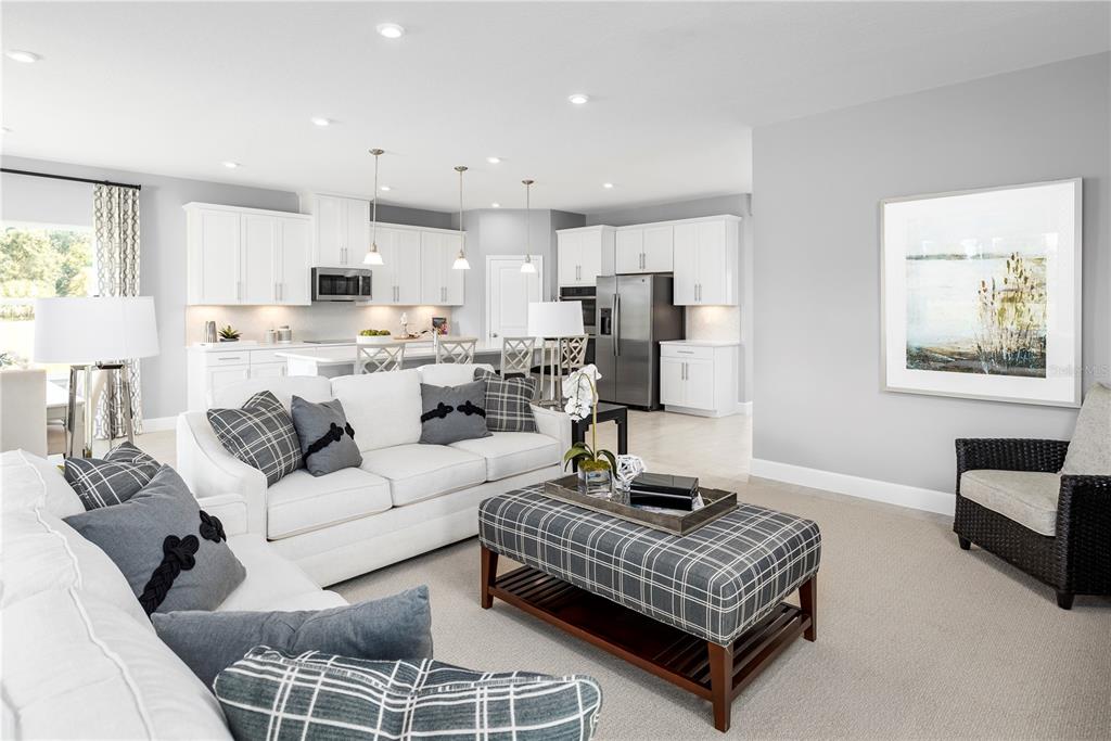 A bright, open-concept living room and kitchen featuring white cabinetry and grey plaid accents — 1726 UPLAND LANE, WINTER HAVEN, FL