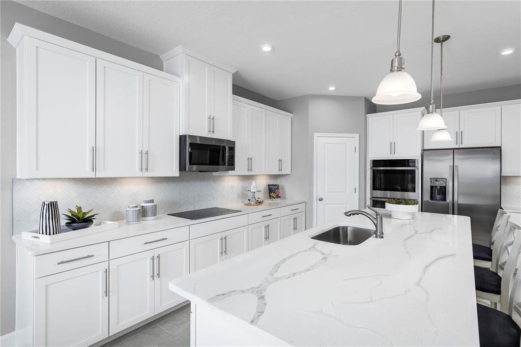 A modern kitchen features white cabinets, a marble-topped island, and stainless steel appliances — 1726 UPLAND LANE, WINTER HAVEN, FL