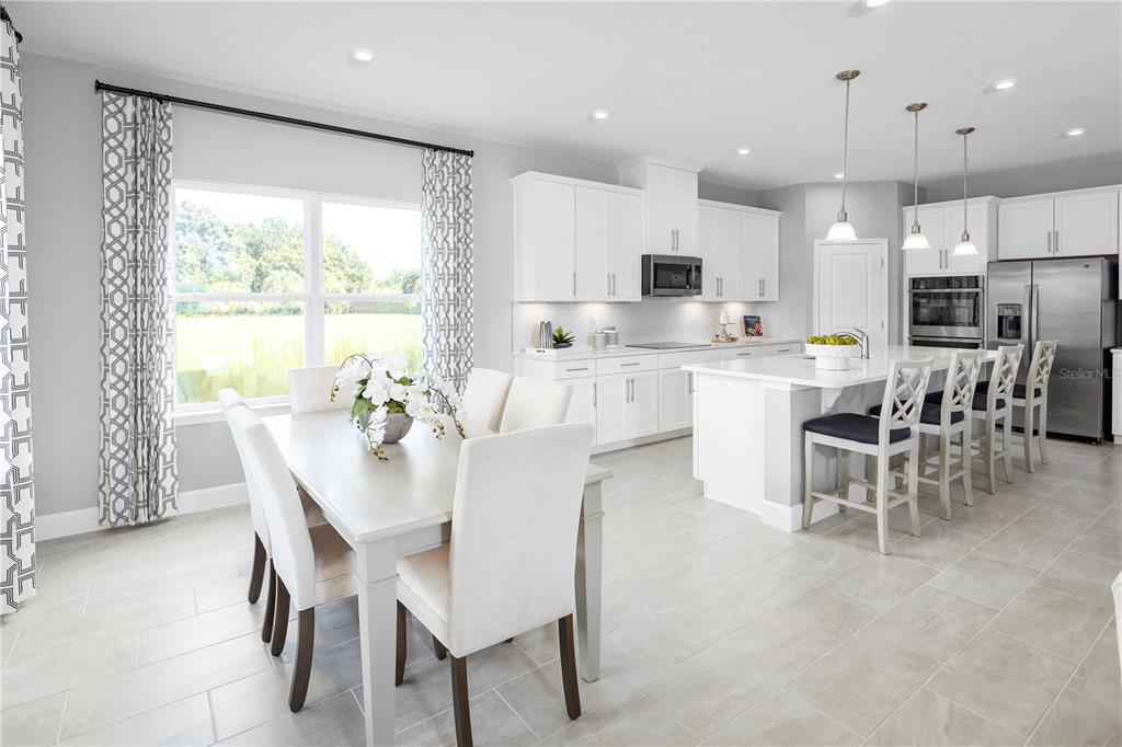A bright, open-concept kitchen and dining area features white cabinetry, stainless appliances, and tile flooring — 1726 UPLAND LANE, WINTER HAVEN, FL