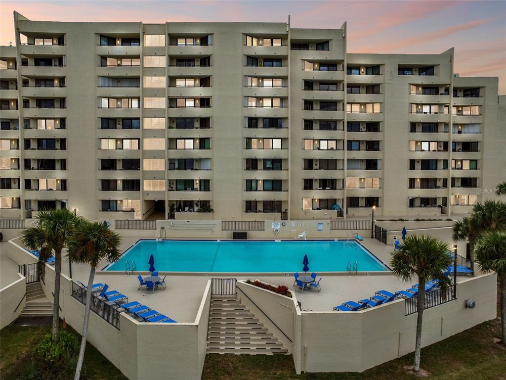 A multi-story apartment building stands behind a rectangular swimming pool with lounge chairs and umbrellas — 5915 SEA RANCH DRIVE UNIT 308, HUDSON, FL