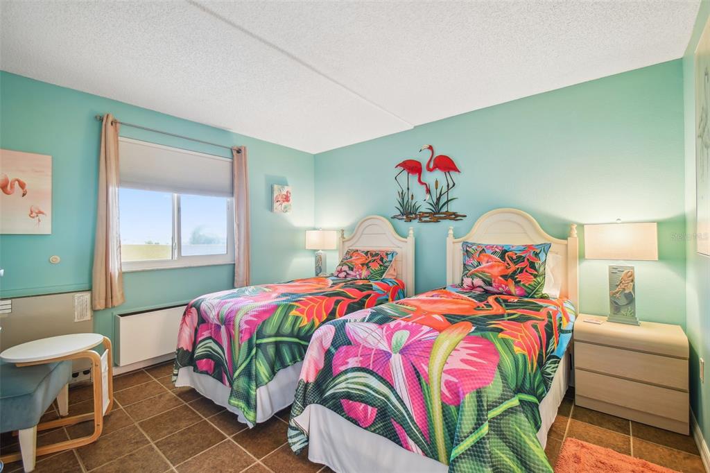 A bedroom features two twin beds with tropical bedding, light blue walls, and tile flooring — 5915 SEA RANCH DRIVE UNIT 308, HUDSON, FL