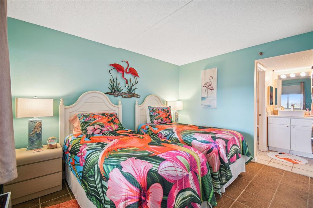A bedroom features two twin beds with tropical flamingo bedding and an attached bathroom — 5915 SEA RANCH DRIVE UNIT 308, HUDSON, FL