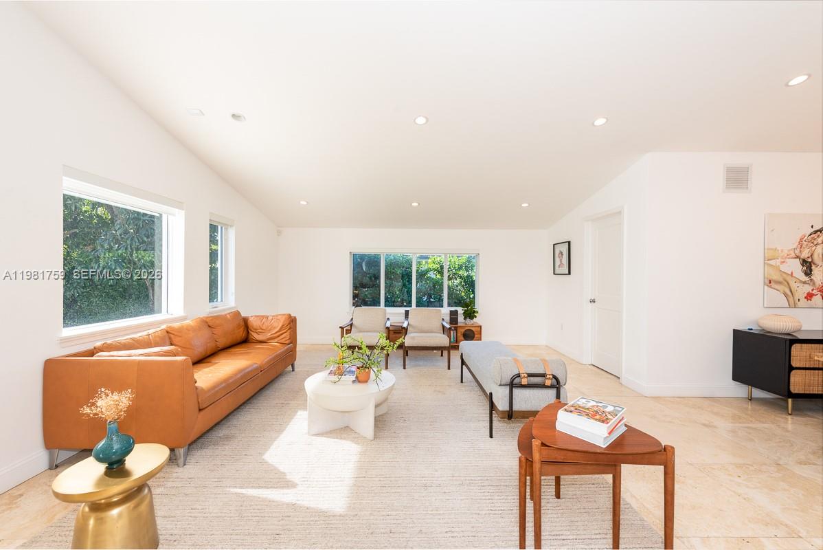 A bright living room features a tan leather sofa, light tile flooring, and large windows — 717 Benevento Ave, Coral Gables FL 33146, CORAL GABLES, FL