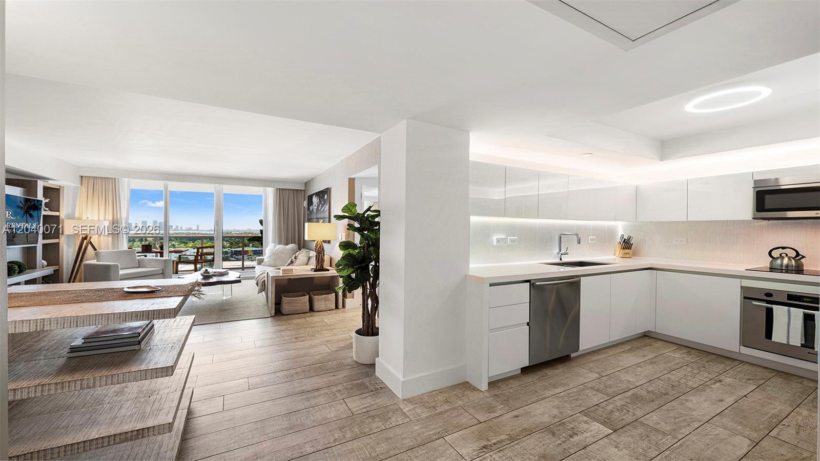 A modern kitchen with white cabinetry and stainless steel appliances opens to a living area — 102 24 # 1545, Miami Beach FL 33139, MIAMI BEACH, FL