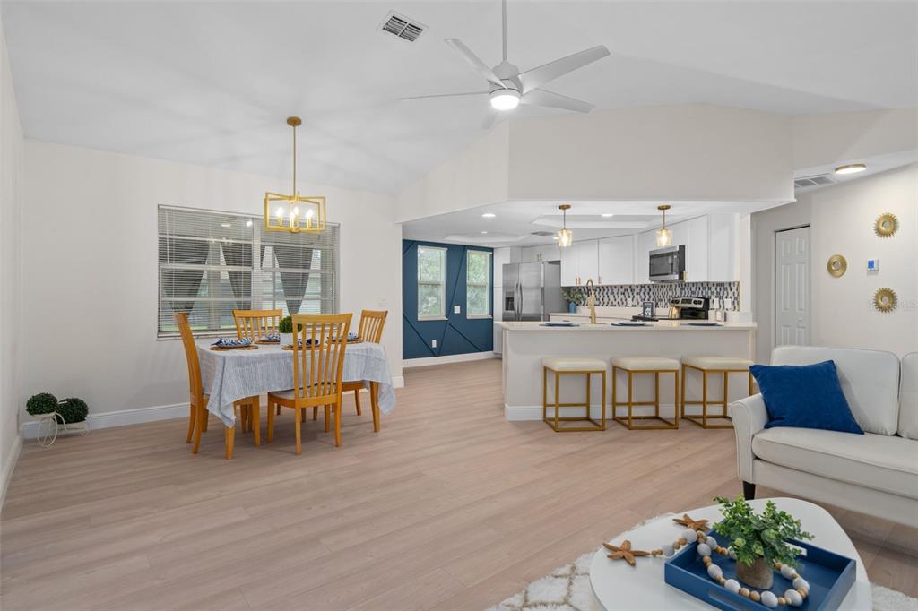 An open-concept living and dining area features light wood flooring, a kitchen island, and furniture — 8643 WOODBRIDGE DR, NEW PORT RICHEY, FL