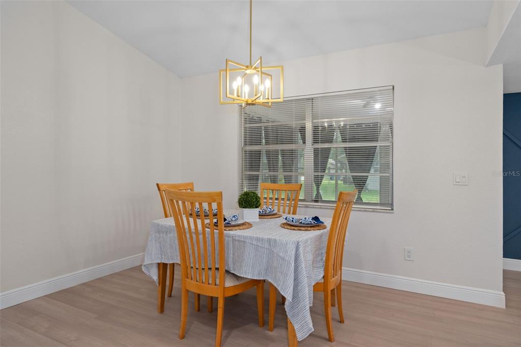 A dining room features a wooden table with four chairs, a light fixture, and blinds — 8643 WOODBRIDGE DR, NEW PORT RICHEY, FL