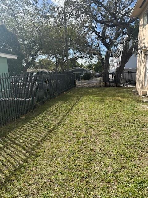 A grassy backyard features a black metal fence and large trees under a blue sky — 14305 NE 6th Ave, North Miami FL 33161, NORTH MIAMI, FL
