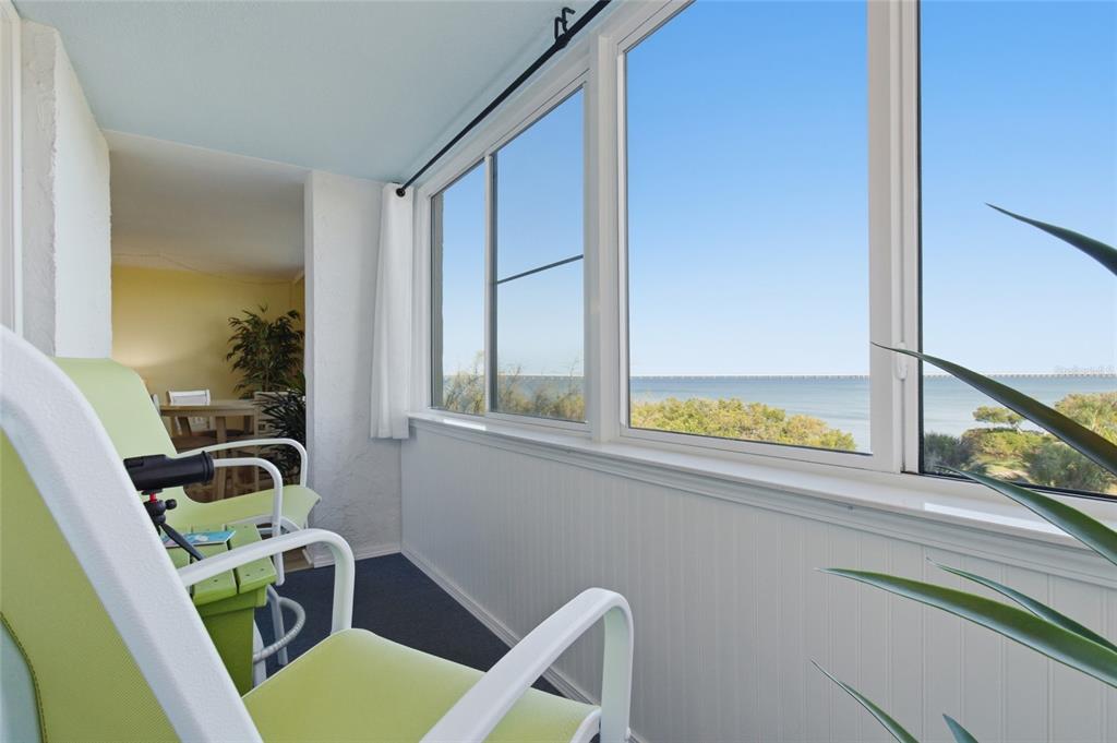 A sunroom features light green chairs, white beadboard walls, and large windows overlooking the ocean — 2616 COVE CAY DRIVE UNIT 502, CLEARWATER, FL