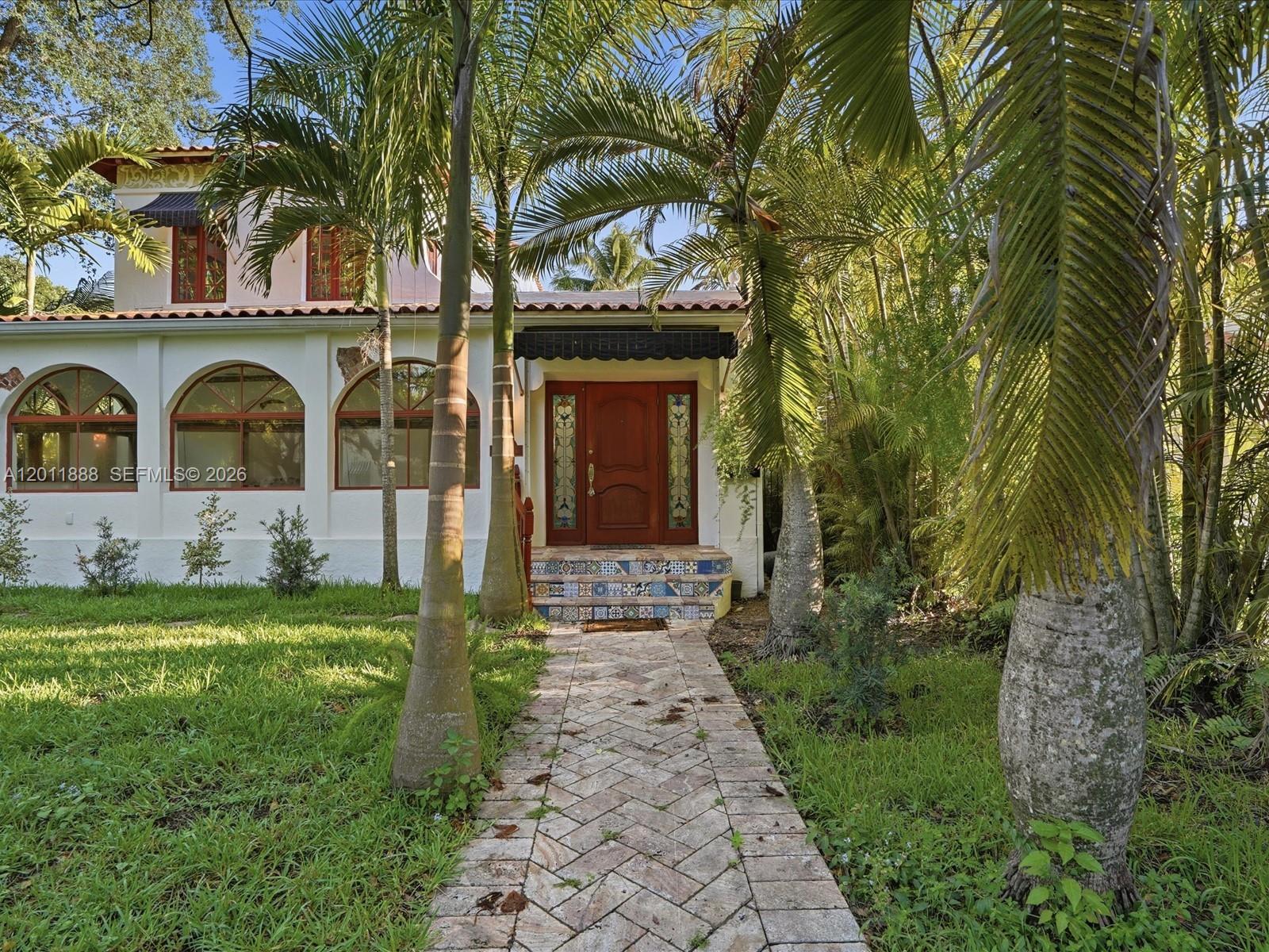 A stone walkway leads to the front entrance of a white house with arched windows — 1137 Asturia Ave, Coral Gables FL 33134, CORAL GABLES, FL