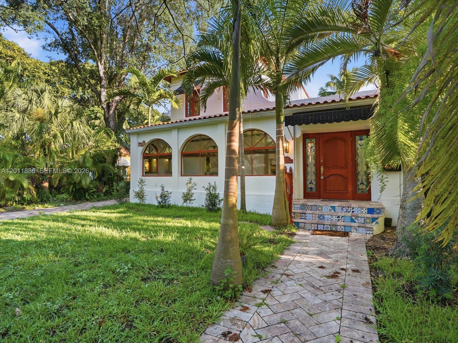 A two-story house with arched windows, a tiled entryway, and palm trees in the yard — 1137 Asturia Ave, Coral Gables FL 33134, CORAL GABLES, FL